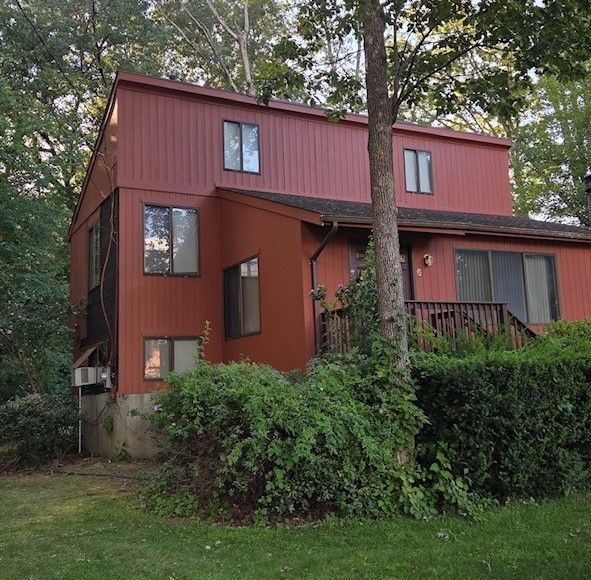 Red two-story house with brown trim, surrounded by trees and shrubs.