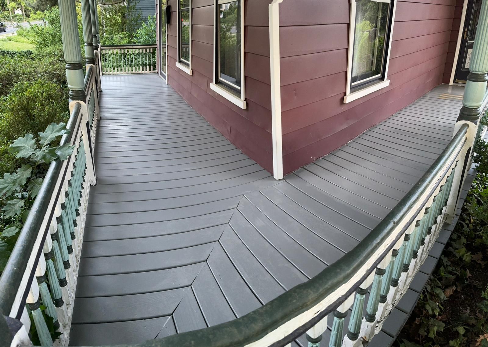 Curved gray deck wrapping around a red house with white-trimmed windows and green railing