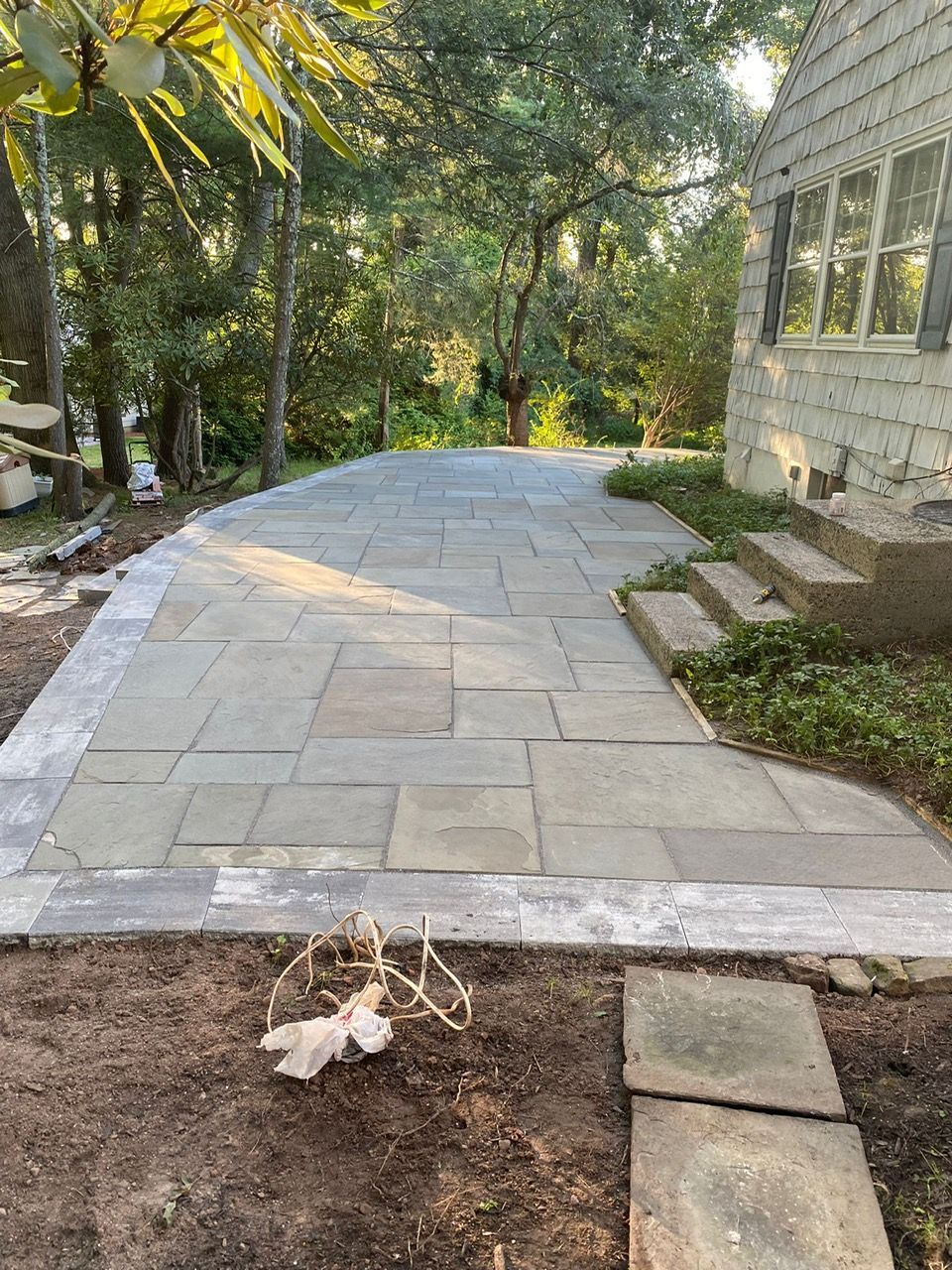 Stone walkway curving through a wooded yard beside a house, with steps and landscaping edging.