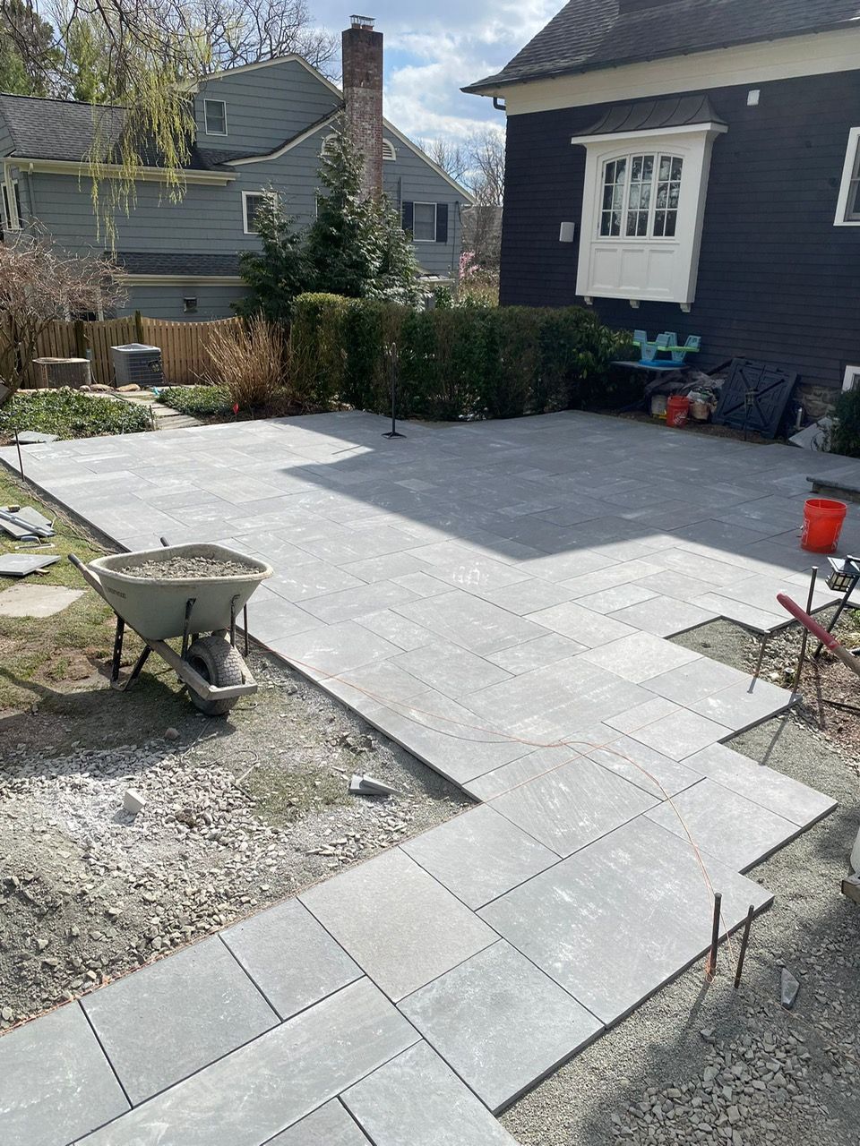 Recently paved gray stone patio beside a house, with a wheelbarrow and red bucket in a backyard.
