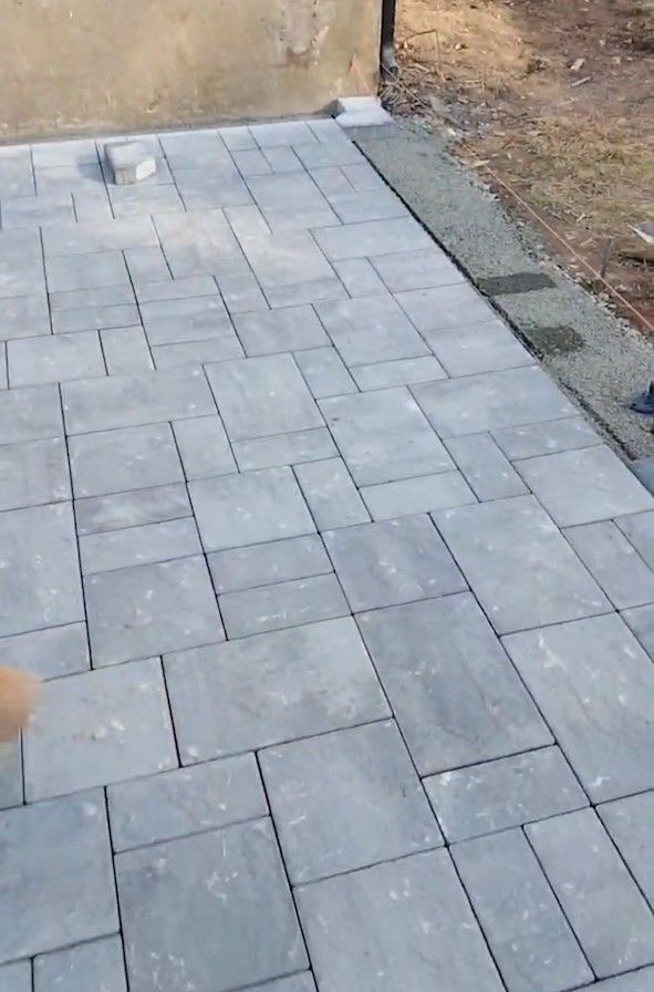 Gray paver walkway beside a dirt edge and narrow concrete border outdoors