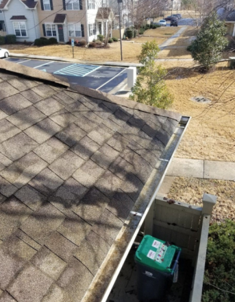 Rooftop gutter and shingles overlooking a suburban yard with a green bin below.