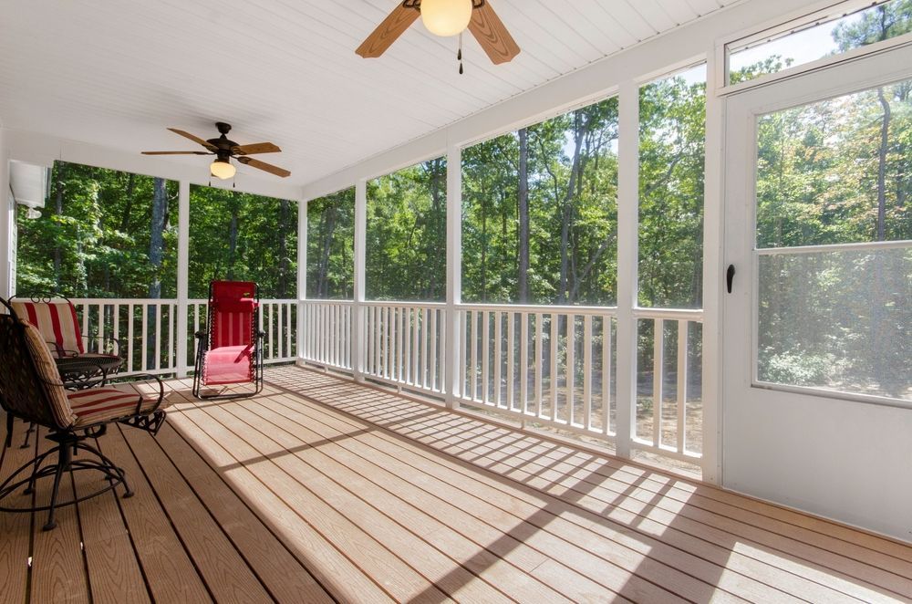 Sunny screened porch with white railings, ceiling fans, and red patio chairs overlooking trees
