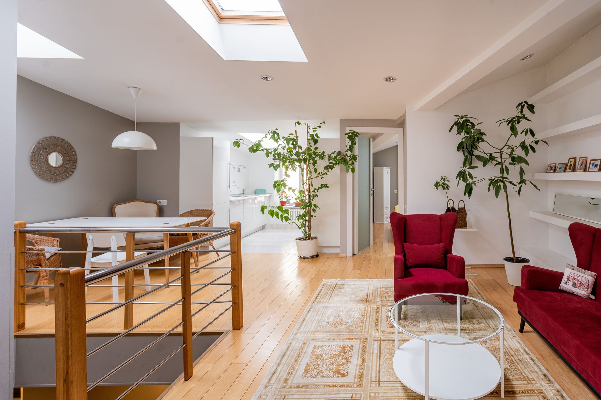 Bright modern living room with red chairs, white sofa, potted plants, and skylight.