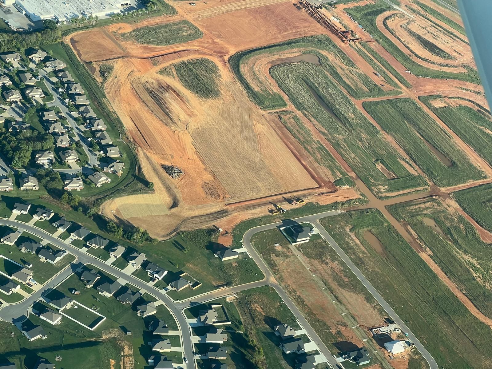 Aerial view of a residential neighborhood bordering a large construction site with cleared land and earthwork.