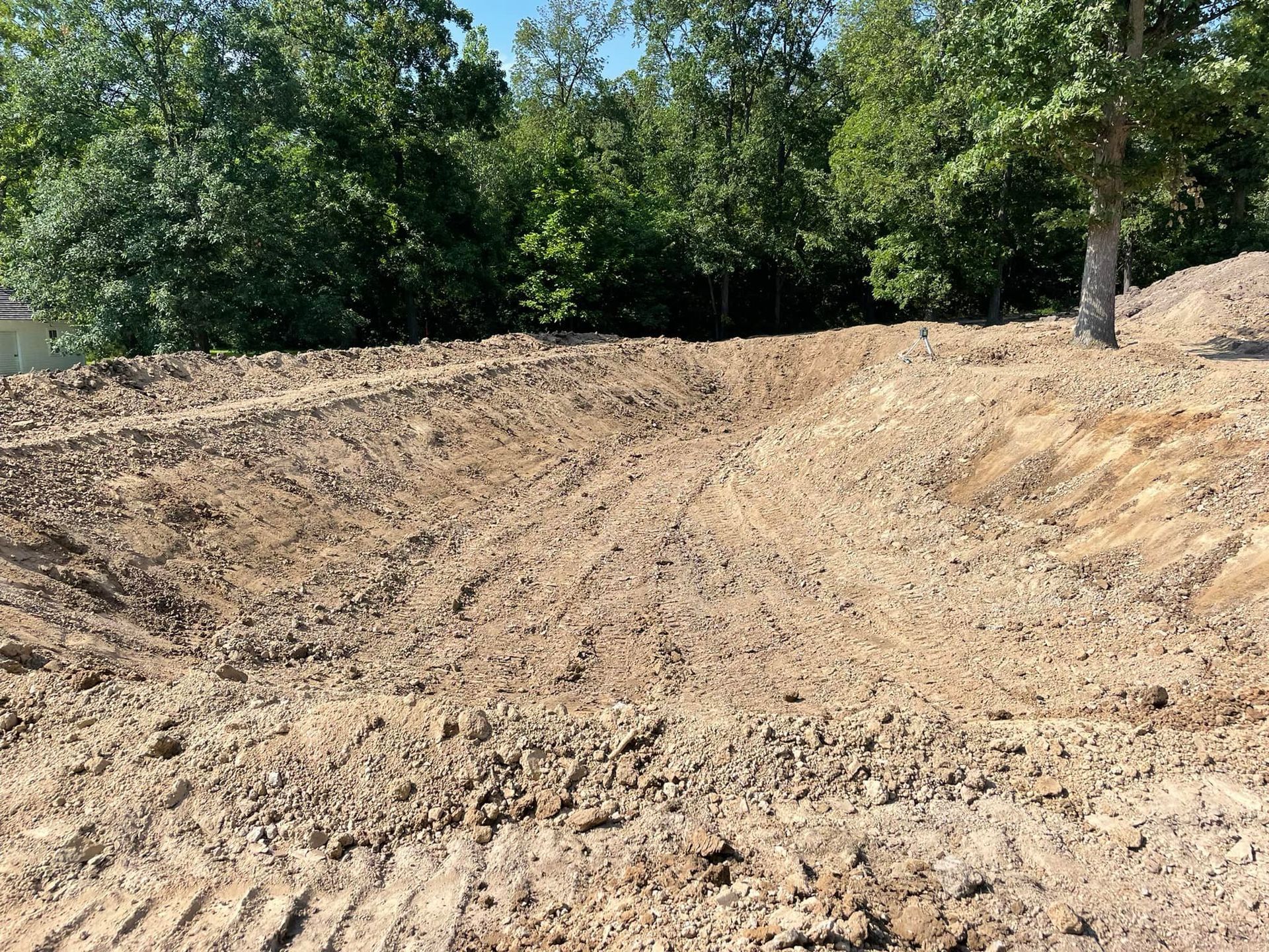 Dirt hill and trenches in a cleared area, trees in the background, daytime.