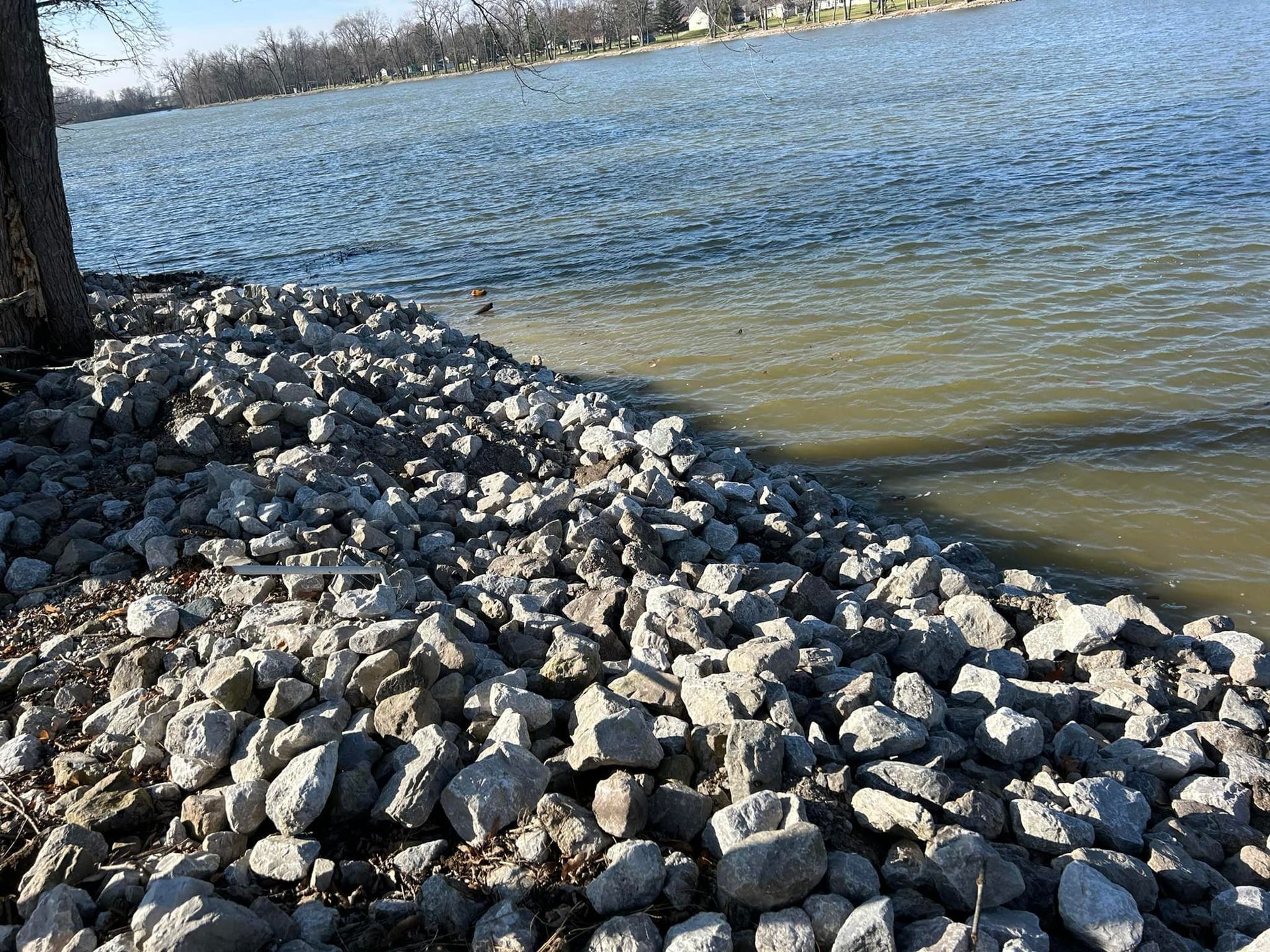 Shoreline protected by rocks next to a body of water on a sunny day.