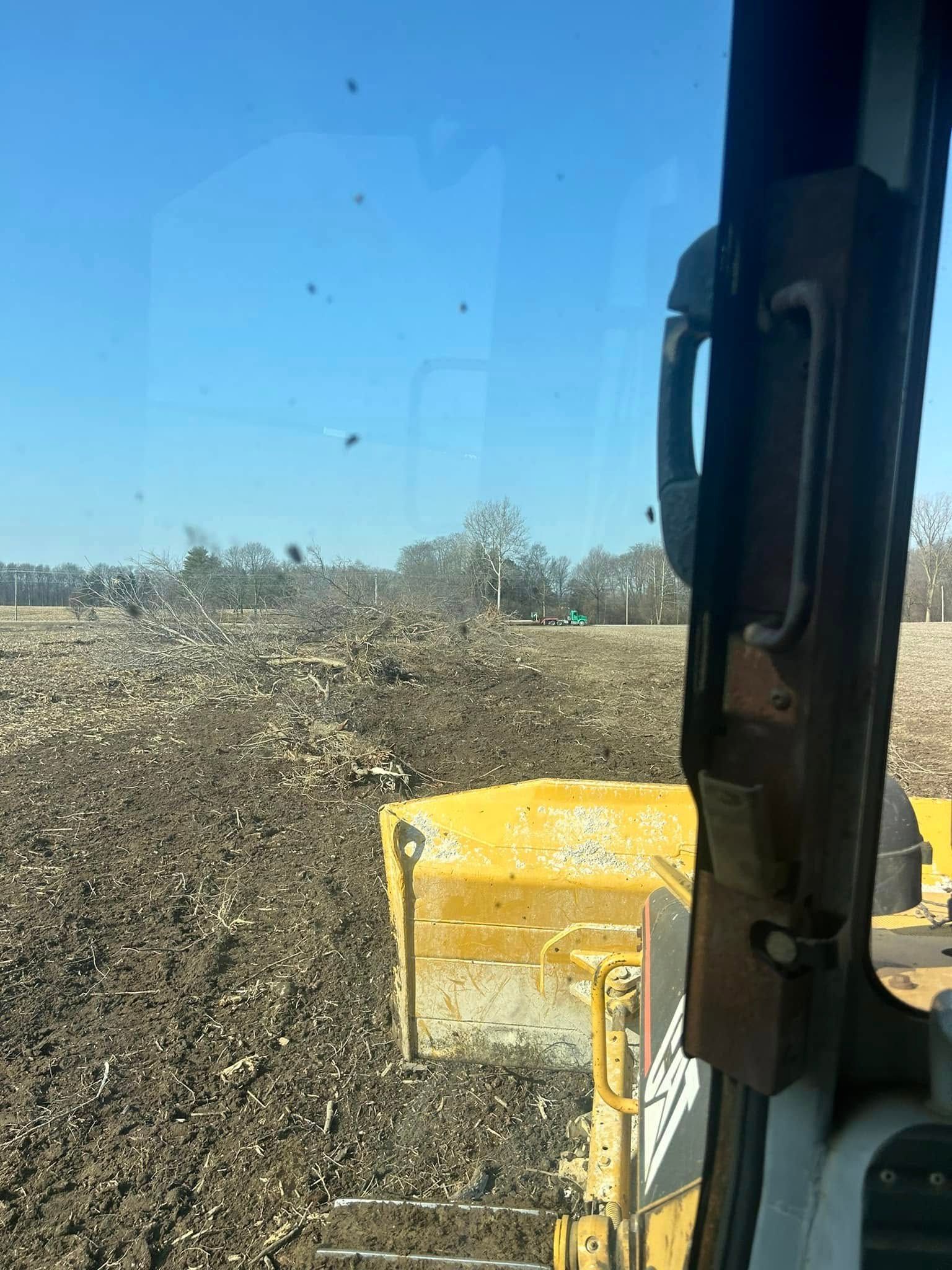View from bulldozer cab; the blade pushes soil across a field under a blue sky.