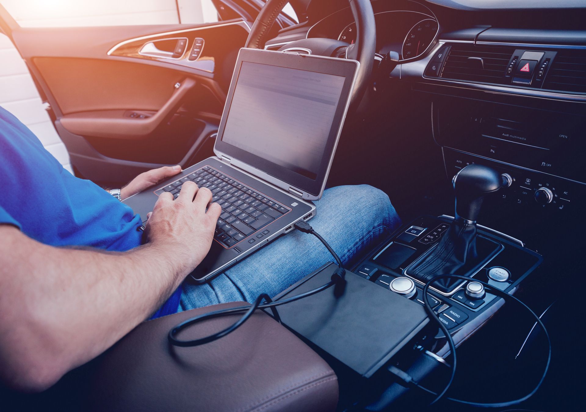 Person in a car, using a laptop on their lap to diagnose vehicle issues.