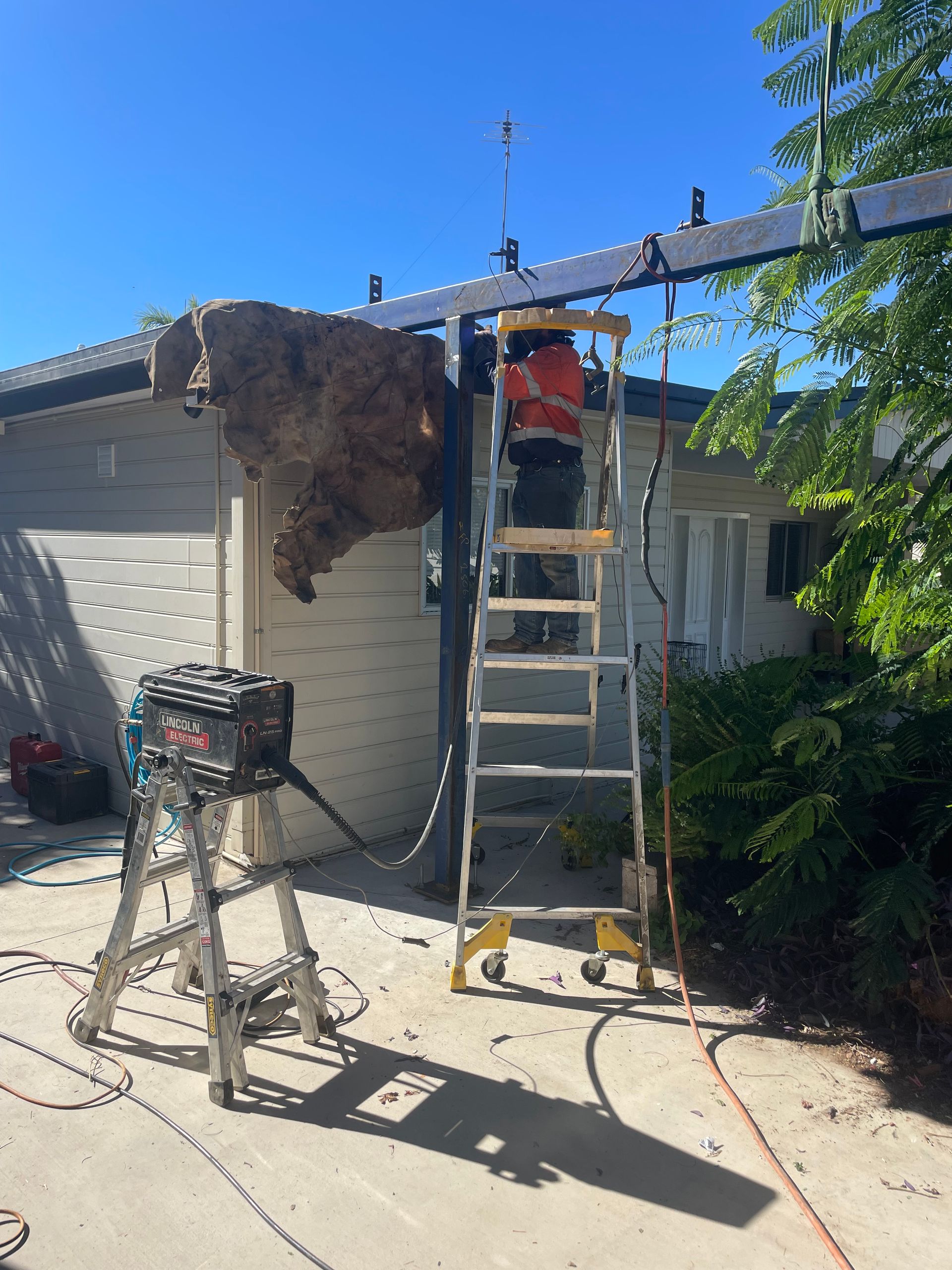 A Person on a Ladder Working on a Large Brown Object Suspended — Lincoln Fabrication in Miles End, QLD