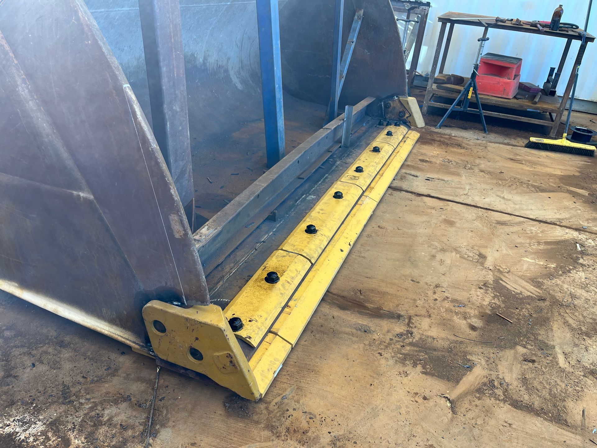 Yellow and grey scoop of a construction machine on concrete floor.