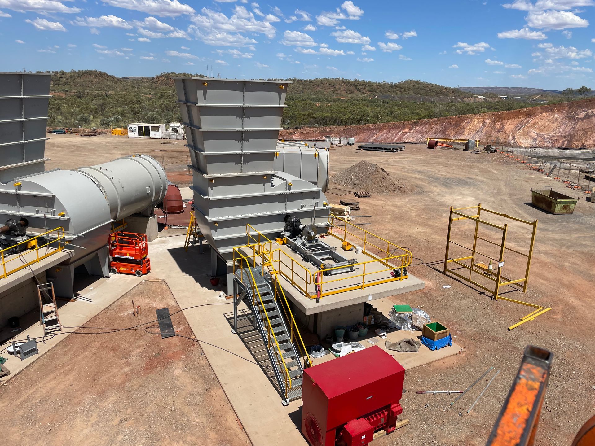 Industrial site with gray machinery, red equipment, and yellow safety rails outdoors.