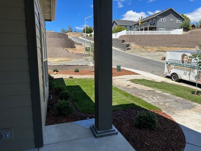 A suburban view from a porch, showing a lawn, landscaping, a paved street, and a truck parked in front of nearby houses.