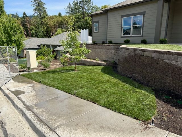 A house exterior with a landscaped front lawn, a newly installed turf area, and a tiered stone retaining wall.