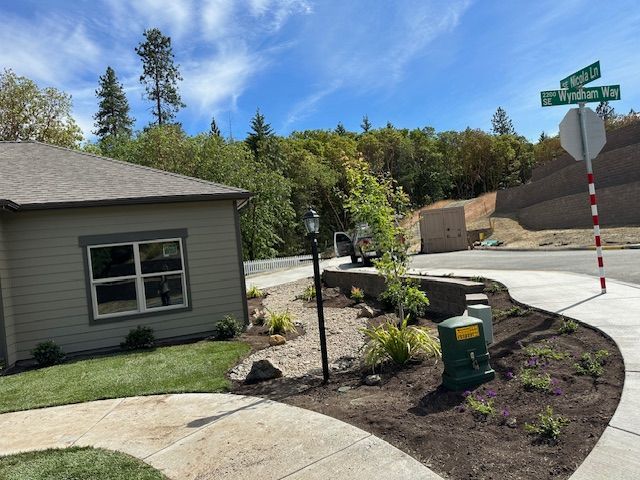 A tan house exterior next to a sidewalk and landscaping with a street sign at the corner on a sunny day.