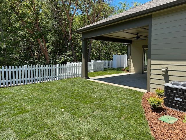 A backyard with a newly sodded lawn, a white picket fence, and a covered patio attached to a green house.