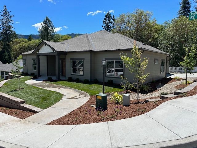 A modern single-story beige house with a grey roof, surrounded by landscaping, green grass, and a curved sidewalk.