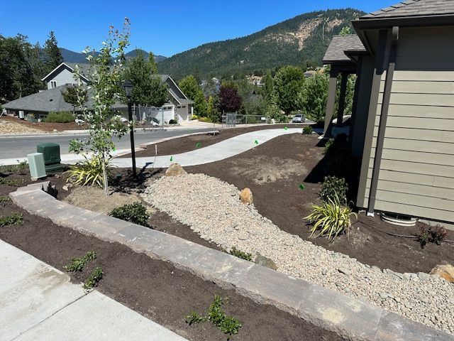 A landscaped front yard features a gravel dry creek bed, a stone retaining wall, new plantings, and a sidewalk.