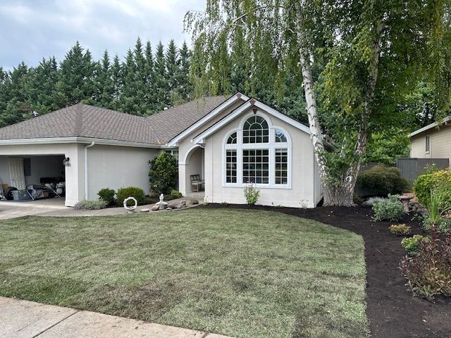 A one-story suburban home with light siding, a large arched window, a two-car garage, and freshly laid grass in the yard.