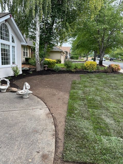 A house exterior with a partially installed lawn, featuring a curved concrete patio edge bordering bare soil and new sod.