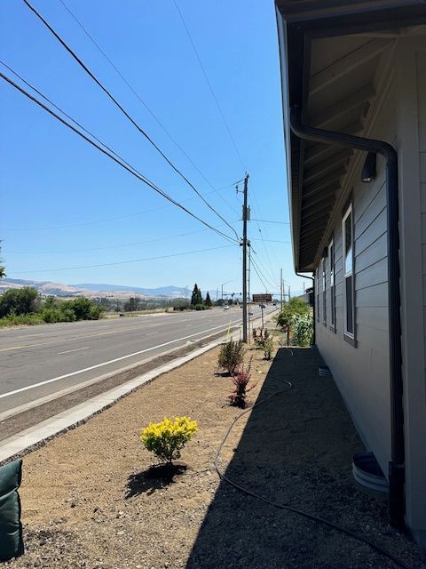 A side view of a building along a highway, with a yellow bush in the foreground and mountains in the distance.
