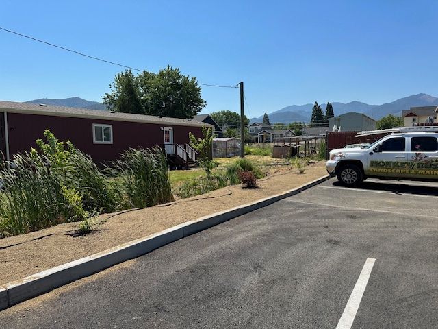 A red mobile home sits next to a paved parking lot with a white service truck parked on the right under a clear blue sky.