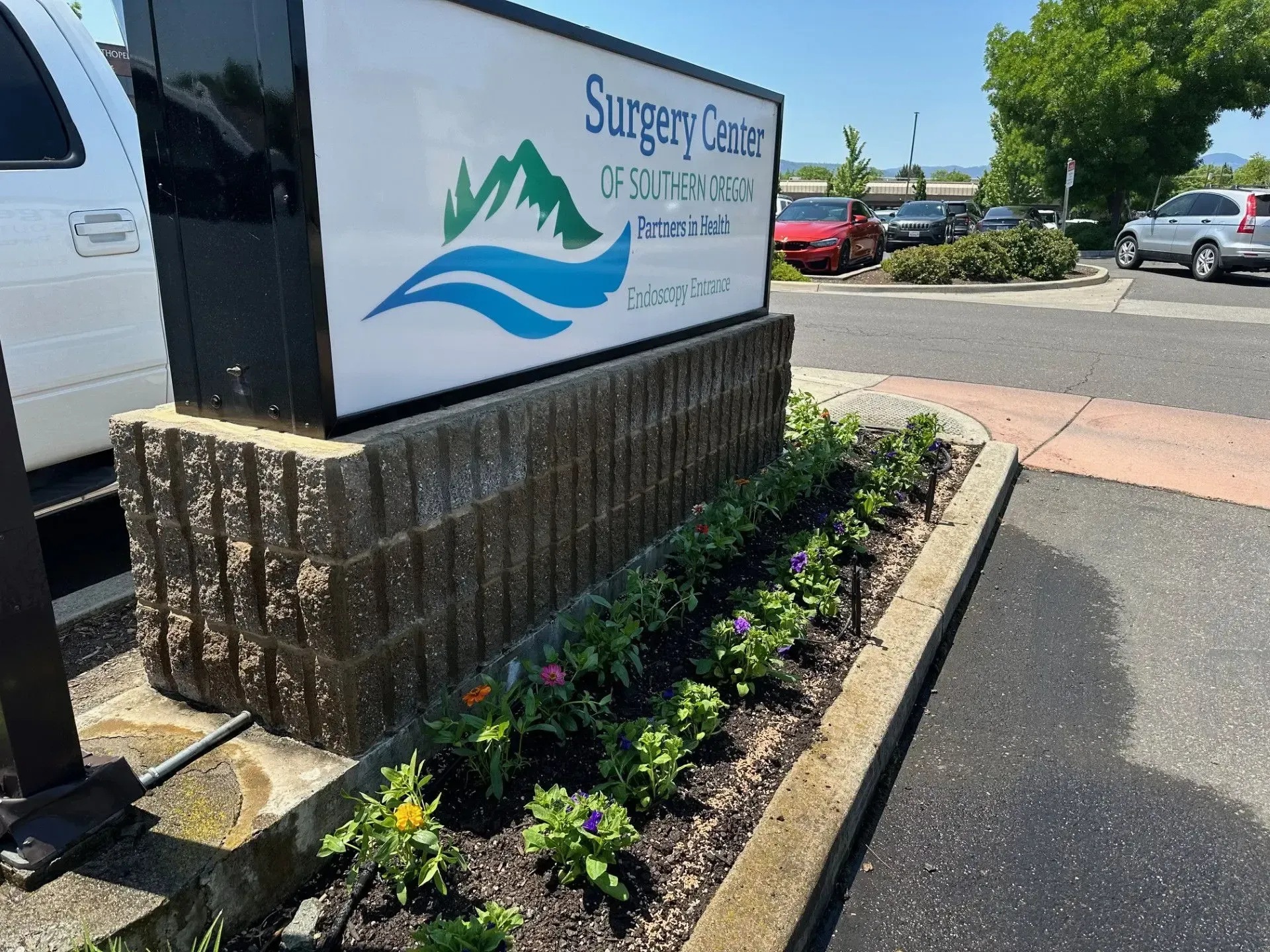 A Surgery Center of Southern Oregon sign standing above a garden bed with small green plants and colorful flowers.