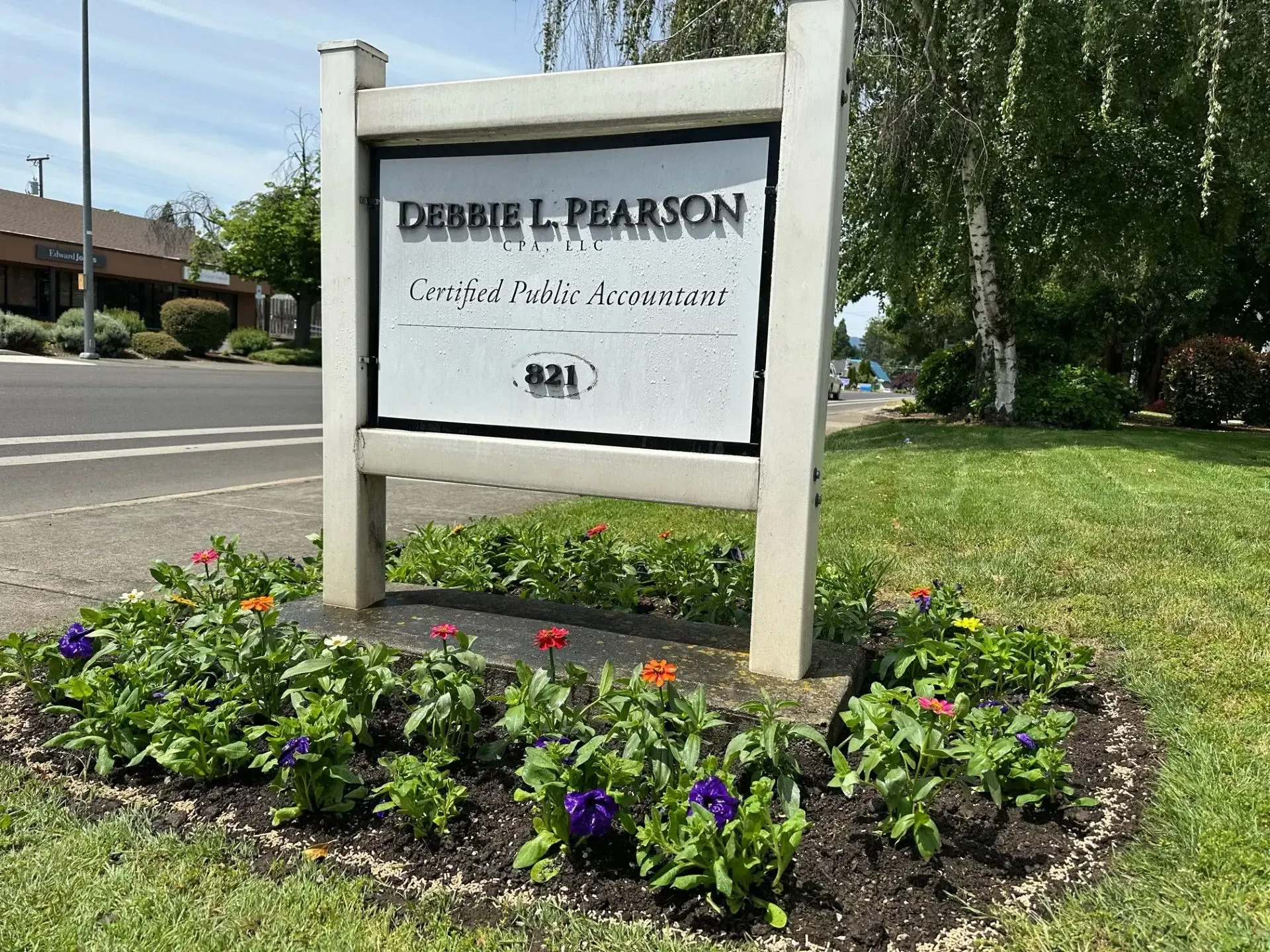 A business sign for Debbie L. Pearson, Certified Public Accountant, set in a garden with colorful flowers.