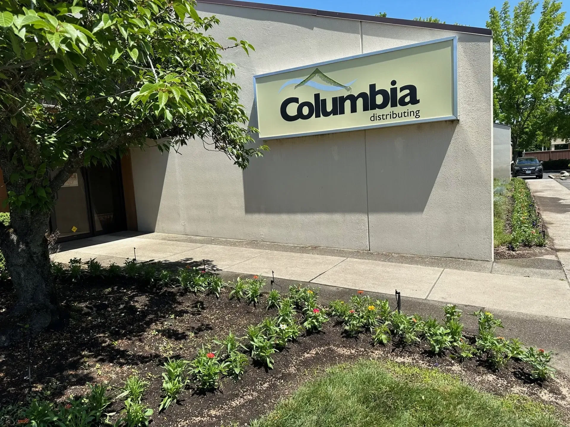 A Columbia Bank building sign on a light-colored stucco exterior with a tree and garden bed in the foreground.