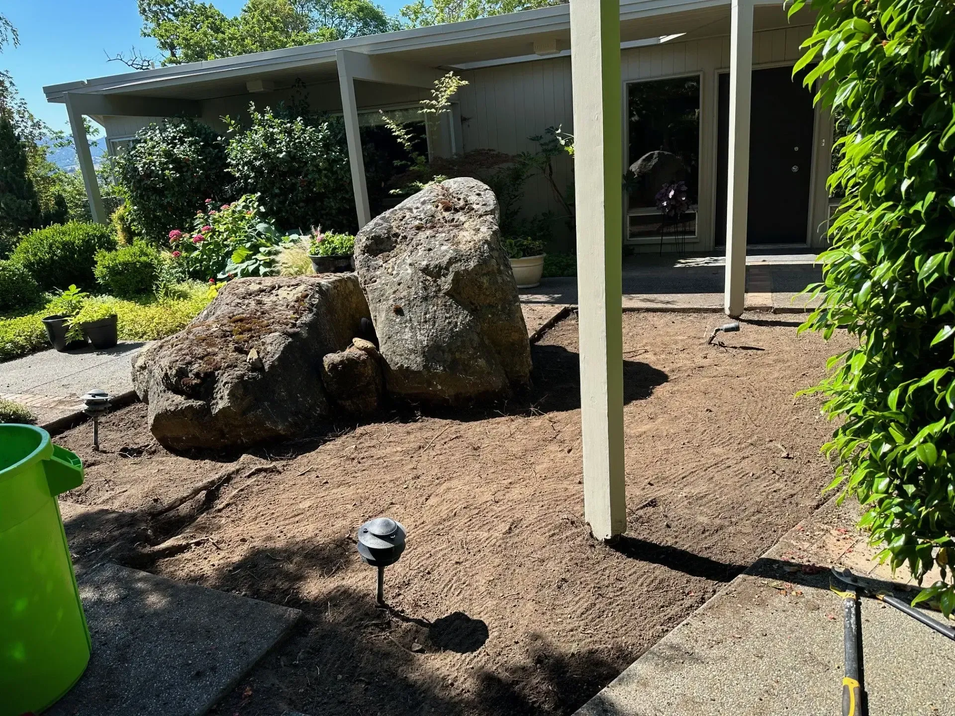 A yard with two large boulders, mulch ground cover, a path, and a porch in the background.