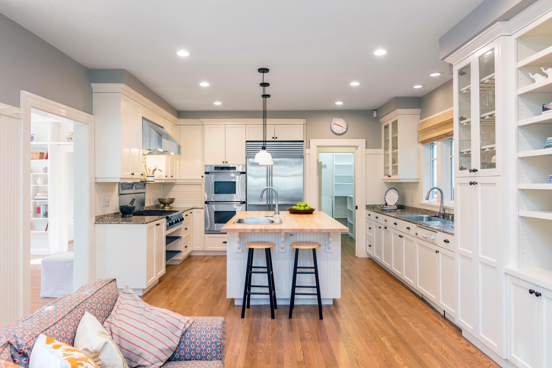 Bright modern kitchen with white cabinets, wood floors, central island, and two bar stools