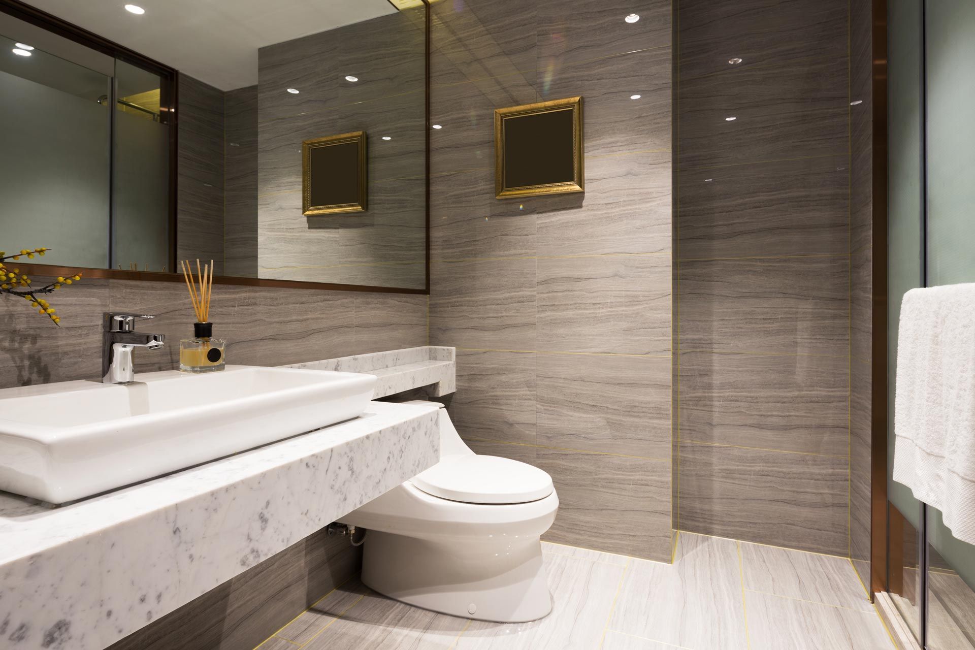 Modern bathroom with marble sink, wall mirror, toilet, and beige tiled walls