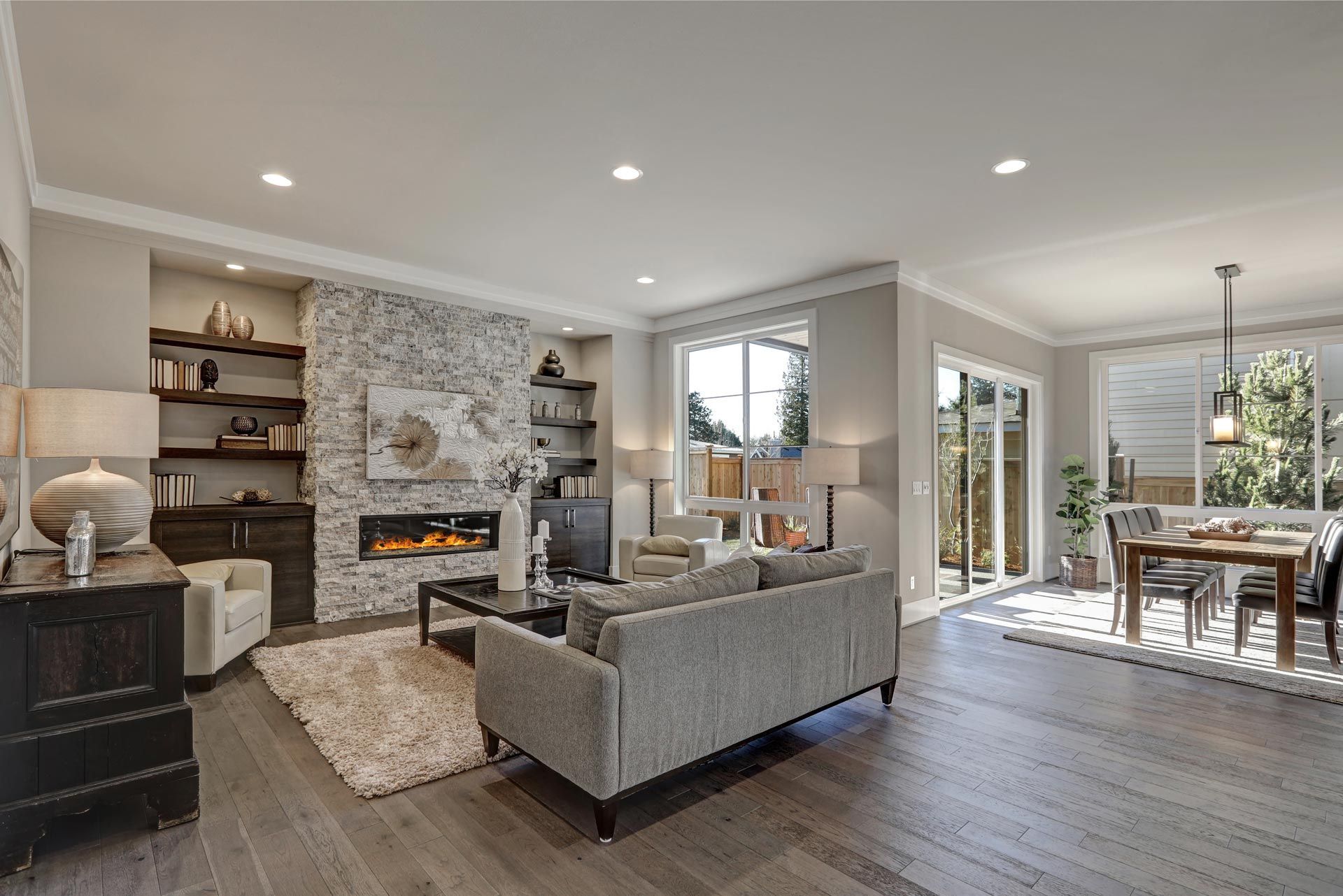 Modern open-concept living and dining room with gray sofas, fireplace, and large windows