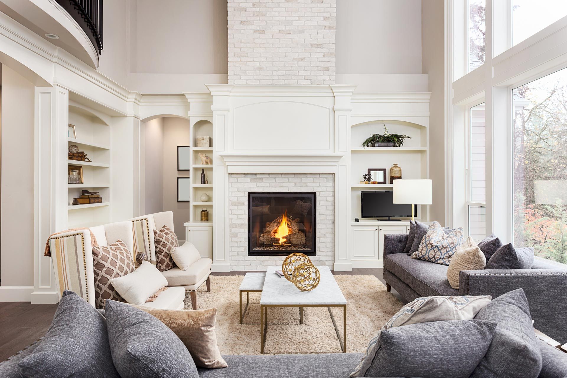 Bright living room with white fireplace, gray sofas, armchairs, and large windows