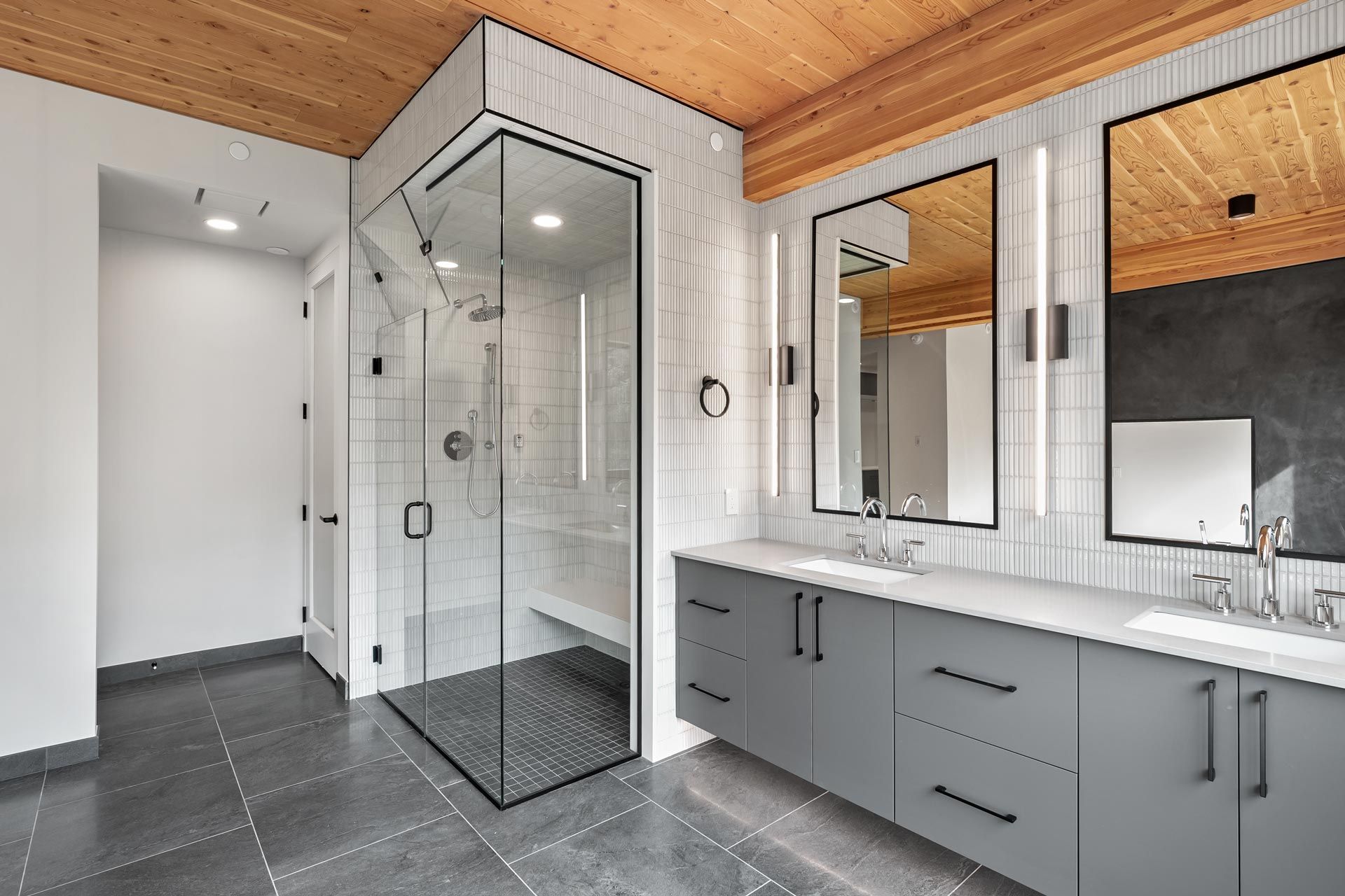 Modern bathroom with glass shower, double vanity, gray tile, and wood ceiling