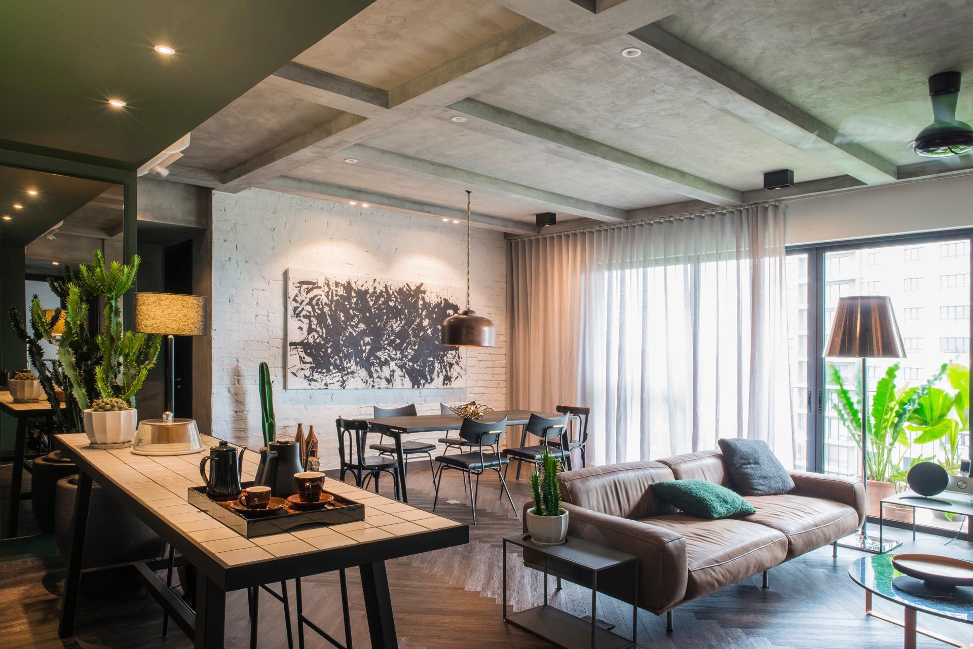 Modern open-plan living room with gray sofa, dining table, large windows, and indoor plants