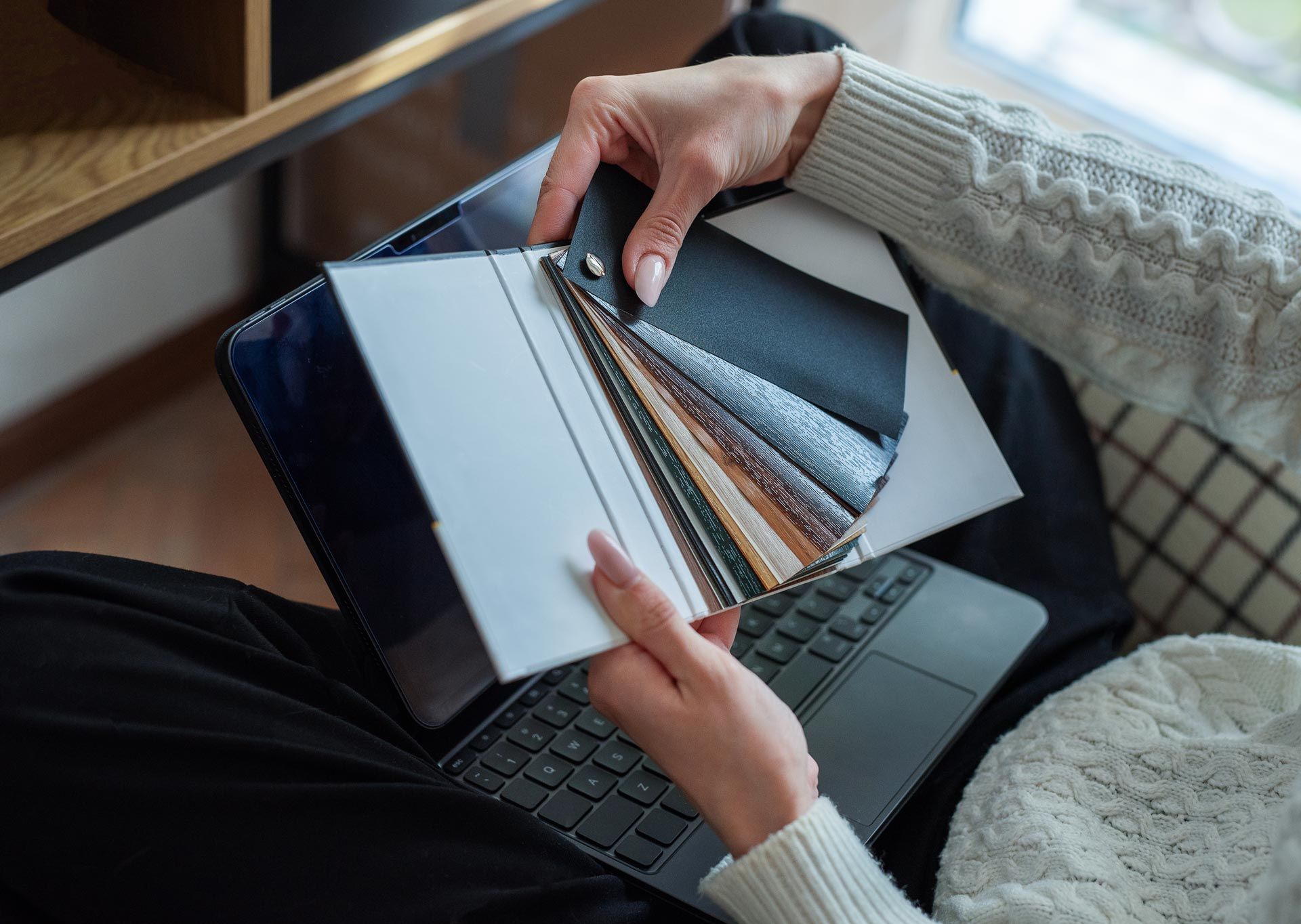 Hands holding open a black case of colorful fabric swatches over a laptop keyboard