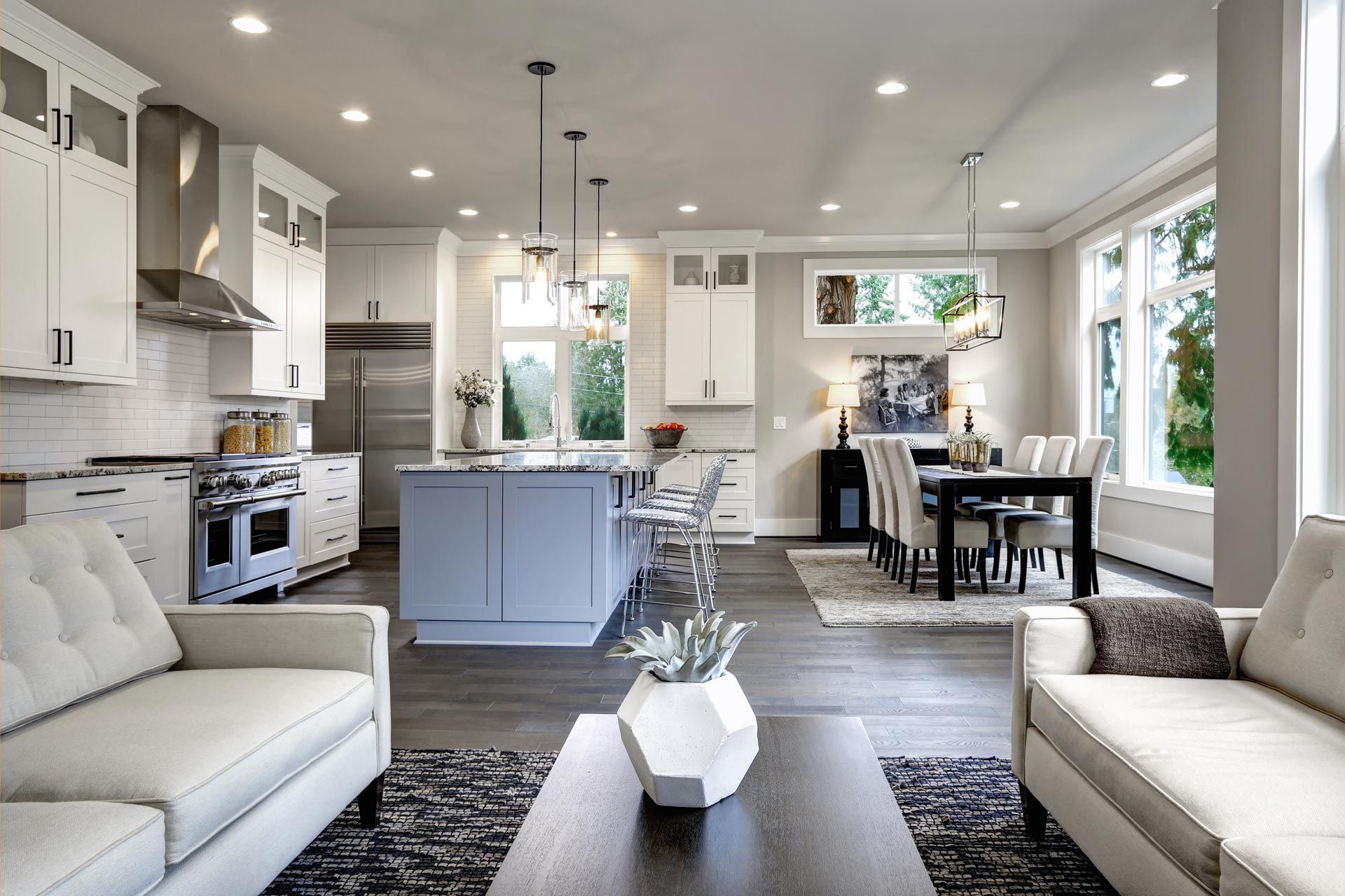 Bright modern open-plan kitchen and living room with white cabinets, island, dining table, and sofas