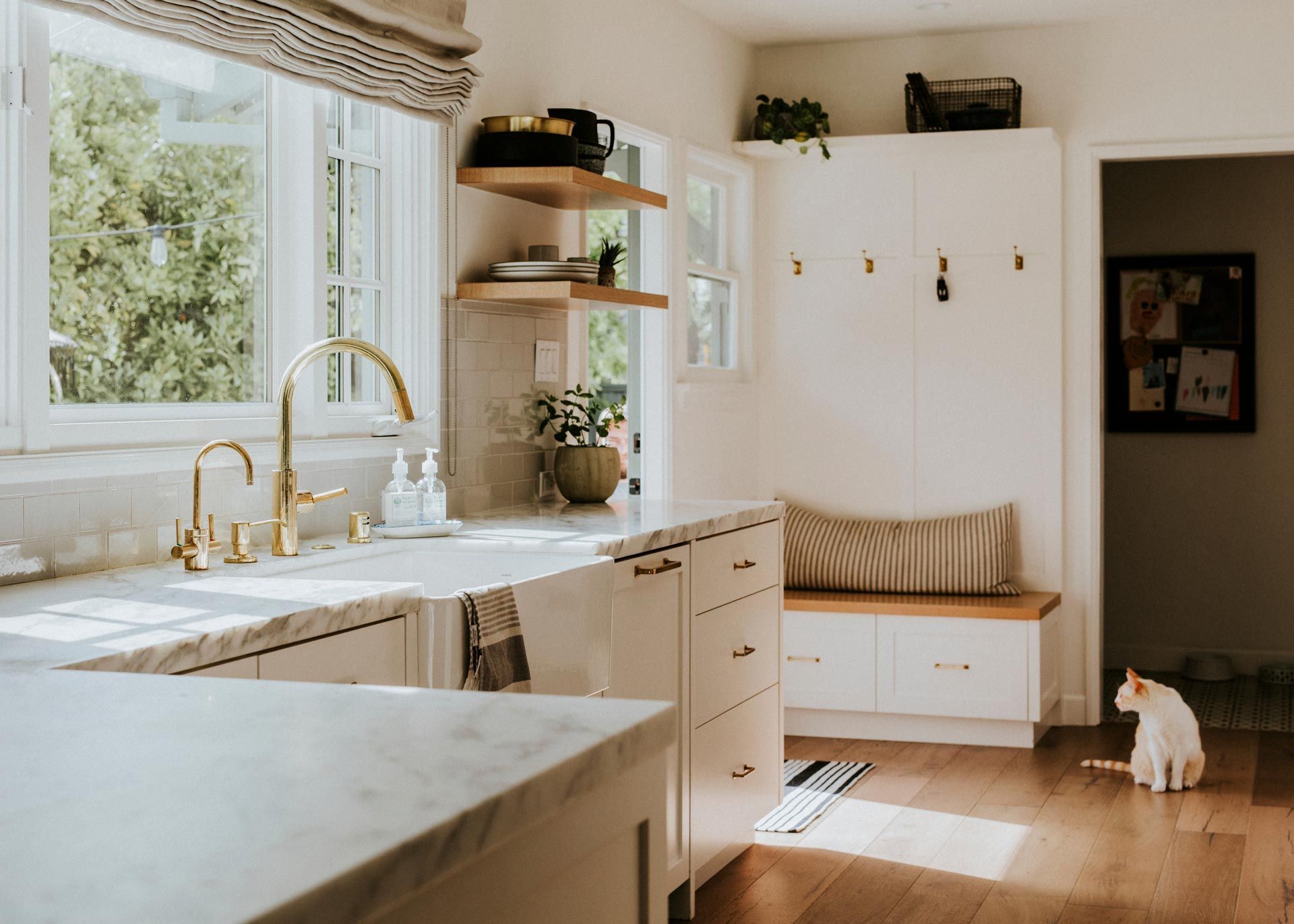 Bright kitchen with white cabinets, brass faucet, window seat, and a small dog by the doorway