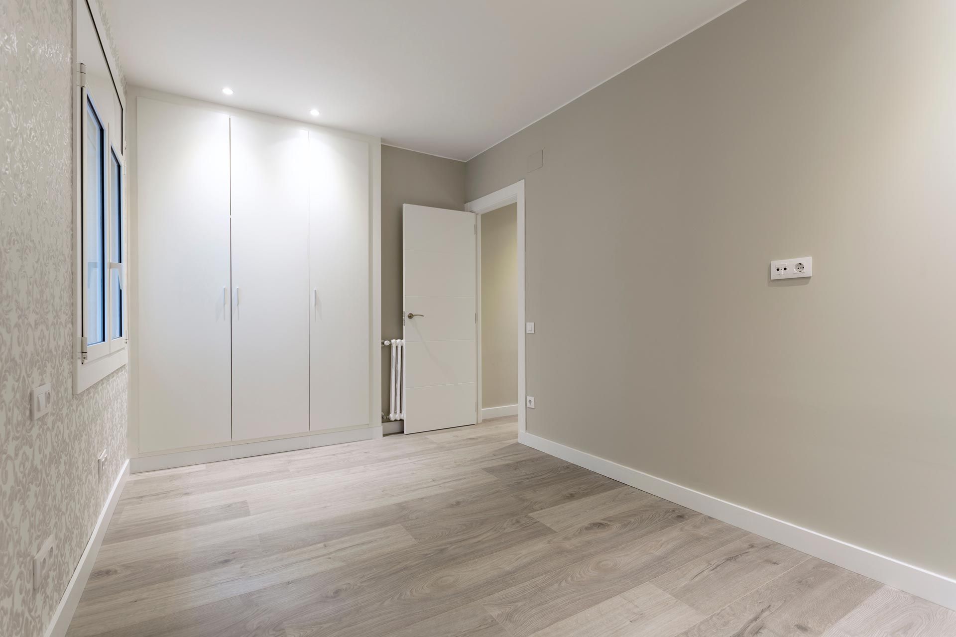 Empty modern room with light wood flooring, white closet doors, and beige walls