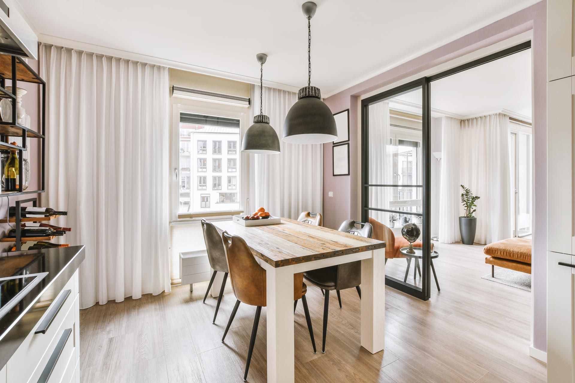 Bright dining room with wooden table, brown chairs, pendant lights, and a view into a white living room