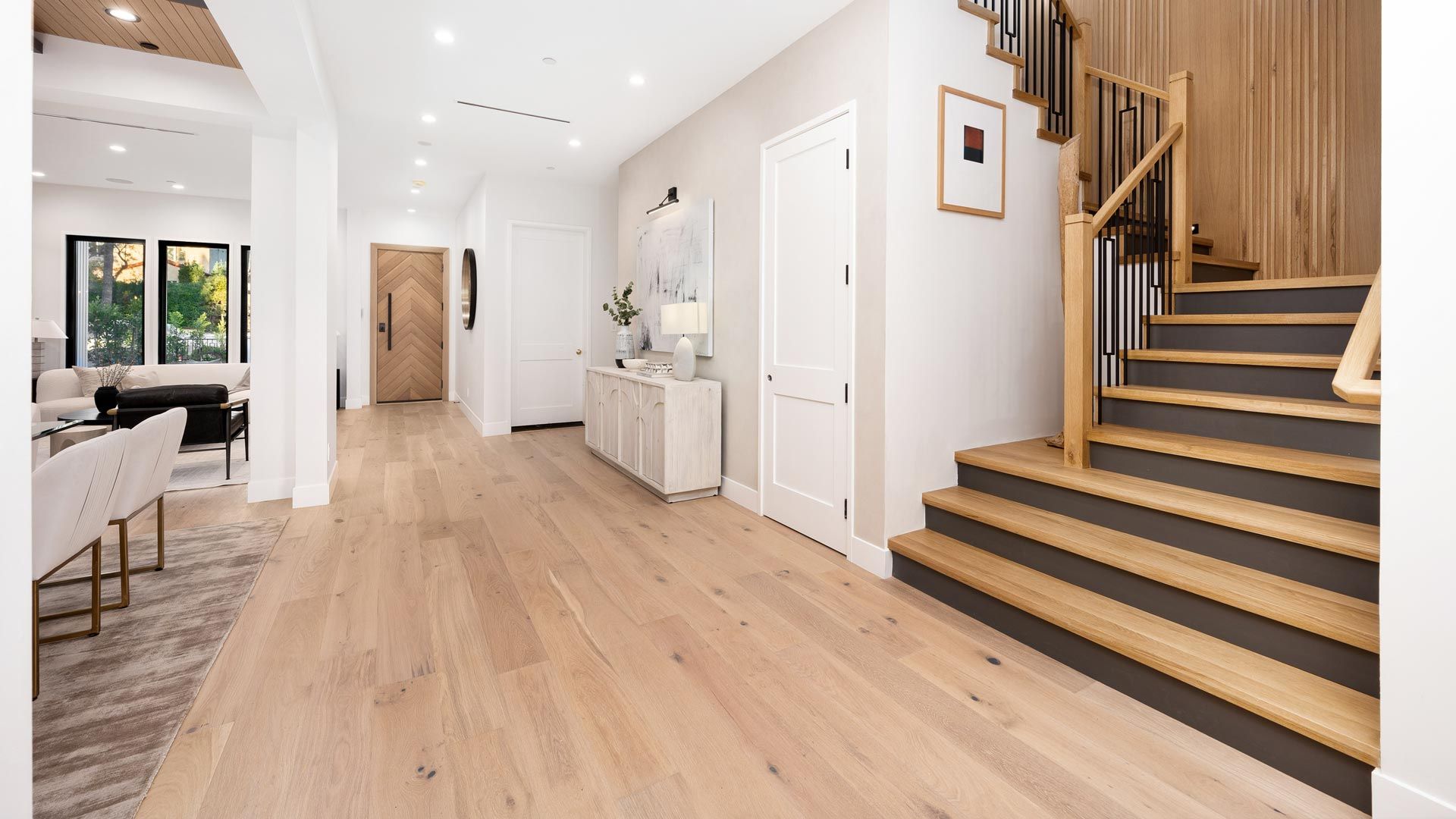 Bright hallway with light wood floors, white walls, and a staircase with black steps and wooden railings