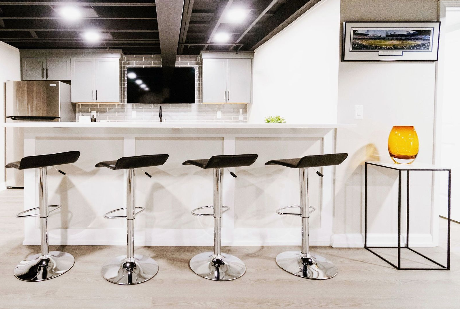 Modern kitchen with wood and white cabinets, marble backsplash, dark dining chairs, and a leafy plant