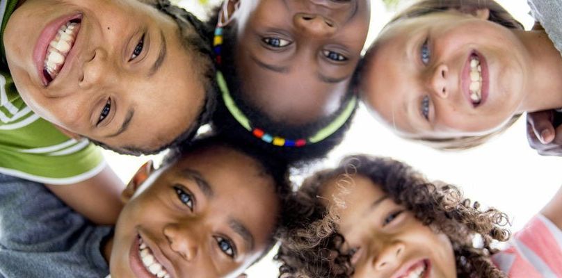 Five smiling children of various ethnicities looking down at the camera in a circle.