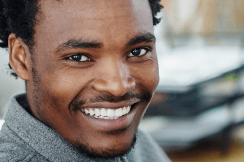 Smiling Black man with a dark mustache, wearing a gray shirt, looking directly at the viewer.