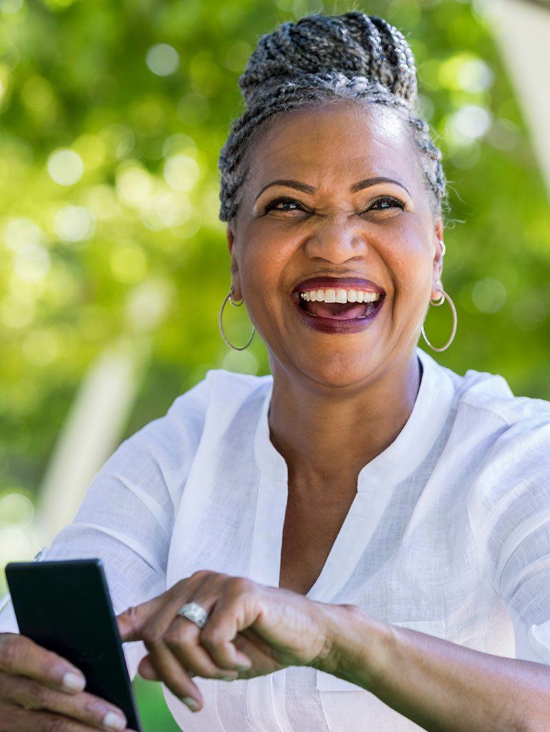 A woman is laughing while holding a cell phone.