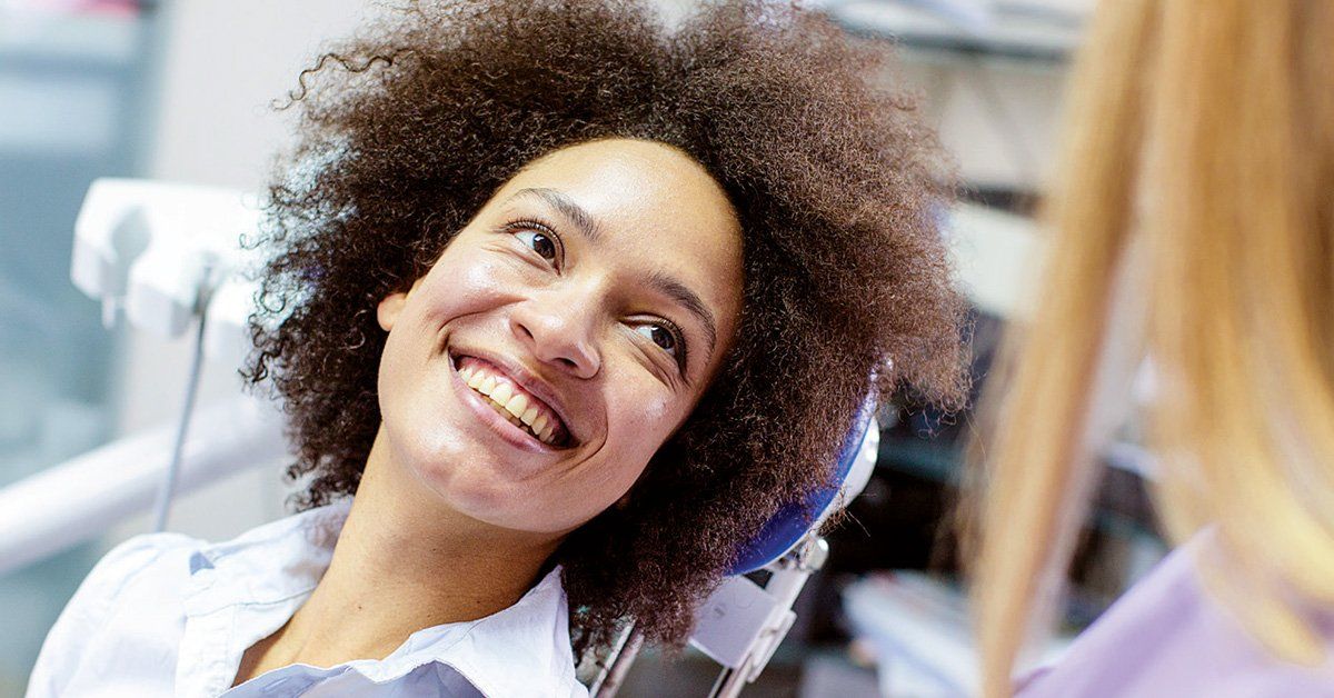 A woman is smiling while sitting in a dental chair.