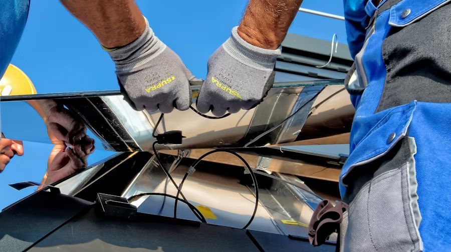 Gloved hands working on cracked black glass or windshield outdoors under a blue sky.