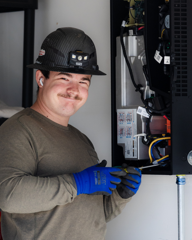 Worker in hard hat and blue gloves using a tool inside an open computer server cabinet.