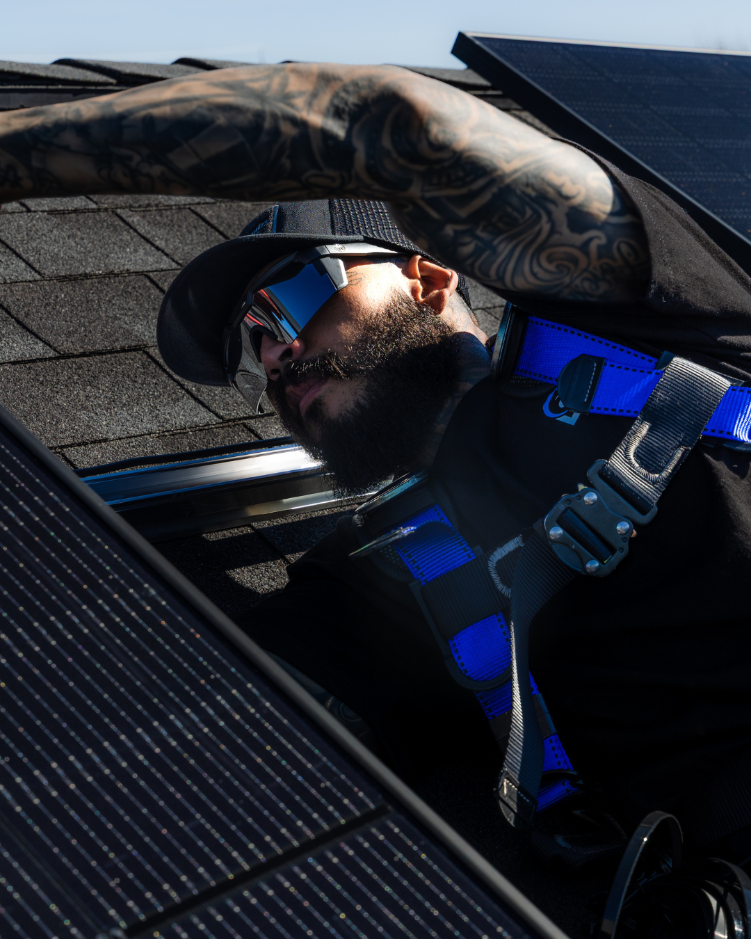 An aerial view of a house with solar panels on the roof Worker in blue harness emerging through a roof hatch, shading his eyes in bright sunlight.